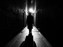 A mysterious man is lurking in a dark alley. A light is shining from behind him, so his face cannot be seen.