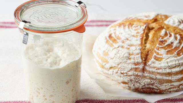 Picture of a jar of sourdough starter and a loaf of round bread