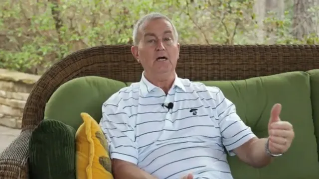 A man wearing a striped polo shirt sits on a wicker couch with green cushions and yellow pillows. He's gesturing with his hand while speaking.