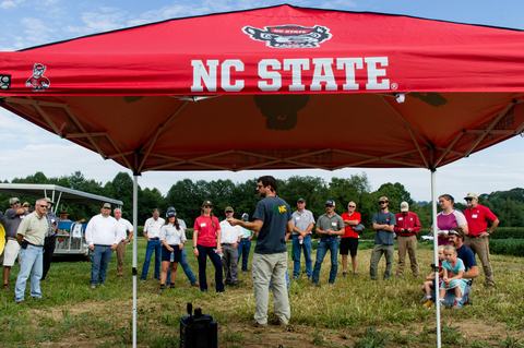 Crowd of people listening to speaker with NC State tent in front