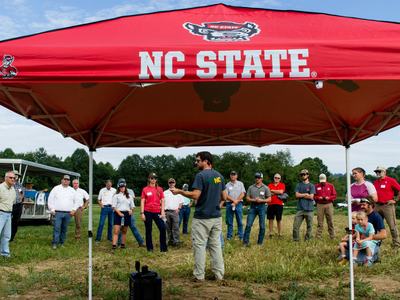 Crowd of people listening to speaker with NC State tent in front
