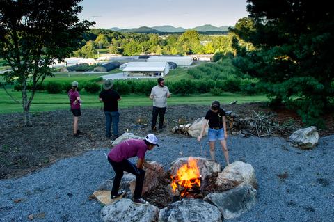 People roasting marshmallows over fire with research station buildings and mountains in background