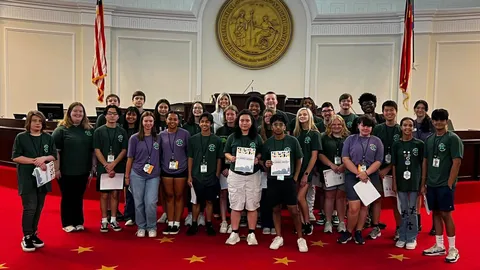 Large group 4-H'ers pose on a red-carpeted chamber floor in the state legislative building as part of a tour during 4-H Congress.