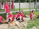 A group of children dressed in red shirts and shorts pose together with a wallaby.