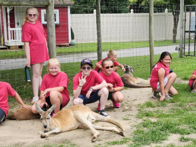 A group of children dressed in red shirts and shorts pose together with a wallaby.