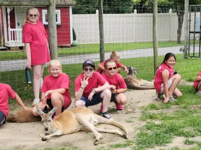 A group of children dressed in red shirts and shorts pose together with a wallaby.