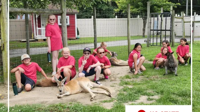 A group of children dressed in red shirts and shorts pose together with a wallaby.