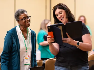 Two women smile while looking at a tablet during a workshop at the North Carolina 4-H Volunteer Leaders' Conference.