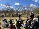 Specialist in red baseball cap talking to group of people in a field adjacent to a river