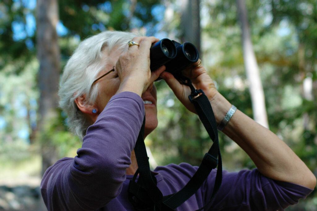 A woman users binoculars to look into the distance.