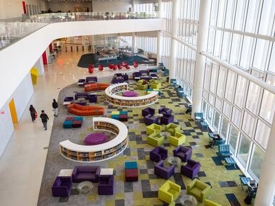 Interior aerial view of NC State University's Hunt Library; a bright and open reading area with colorful chairs and bookshelves in front of a wall of windows looking out on Centennial Campus.