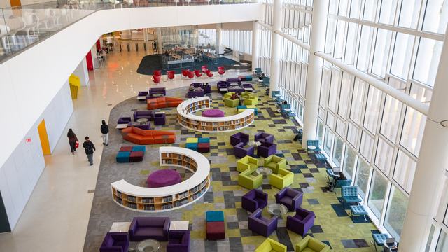 Interior aerial view of NC State University's Hunt Library; a bright and open reading area with colorful chairs and bookshelves in front of a wall of windows looking out on Centennial Campus.