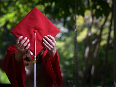 Youth holding red graduation cap.