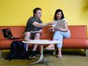 Two young people-one male, one female-sitting on a couch.  One holding a computer with the other pointing someting out on the computer.