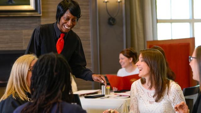 Server standing and interacting at a table with three patrons sitting.