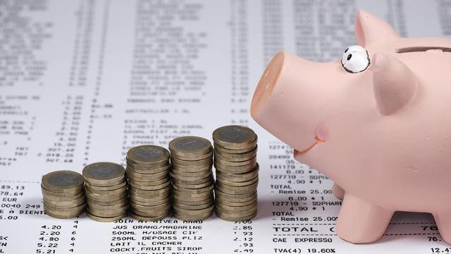 Piggy Bank is facing toward five rows of coins stacked on top of grocery receipts.