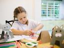 A small girl is completing a craft on a table covered in craft supplies, such as paper and scissors.