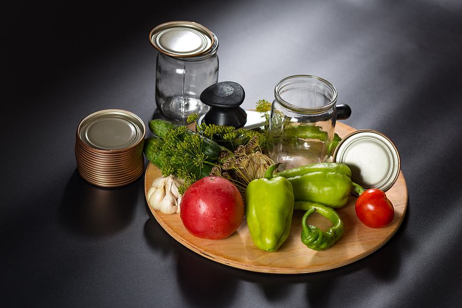 Empty Mason jar surrounded by tomatoes, peppers, garlic, herbs and canning lids lids
