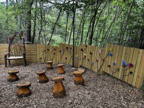 Outdoor book nook.jpg with mushroom stools, decorative fence, and wooden bench in the woods.