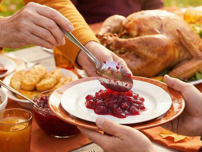 Turkey dinner on table.  Person spooning cranberries onto plate.