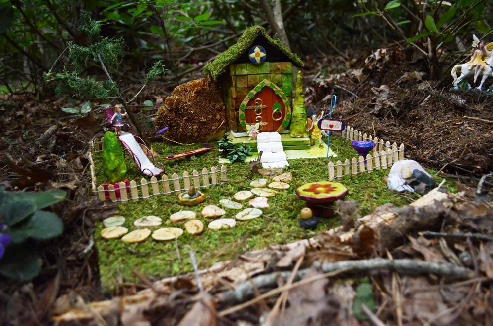 Mini fairy house in the woods with a moss roof, path, and picket fence