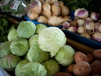 A display of fresh fall produce at a market, including heads of green cabbage, purple-top turnips, parsnips, and sweet potatoes.