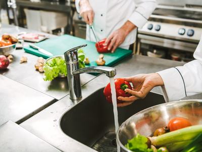 Kitchen where vegetables are being washed and all chefs are following food safety rules.