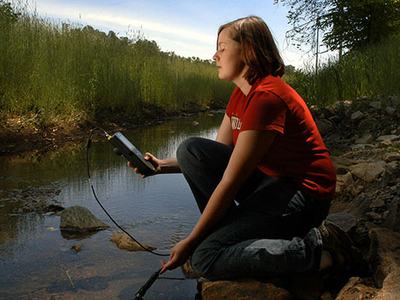 Woman analyzing water quality in a stream