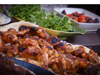 Grilled chicken on a plate with green salad and cut fruit and fruit pastry in the background on the table.