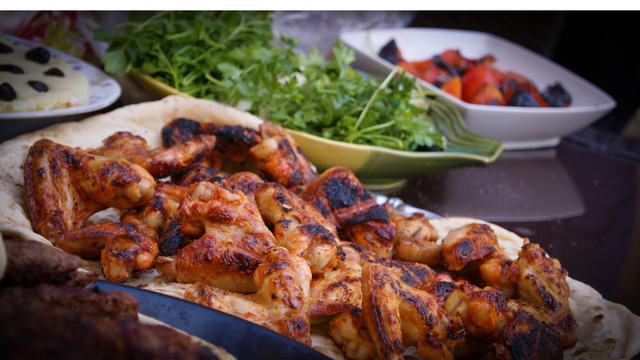 Grilled chicken on table with green salad, fruit salad and fruit pastry in background.