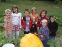 A group of youth standing behind a giant pumpkin in a field.