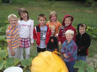 A group of youth standing behind a giant pumpkin in a field.