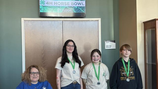 3 kids standing and wearing a medal and an adult in a wheelchair