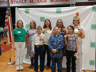 Stanly County 4-H Agent, with 7 Stanly 4-H youth who participated in District presentations.  They are posed in front of a 4-H logo backdrop.