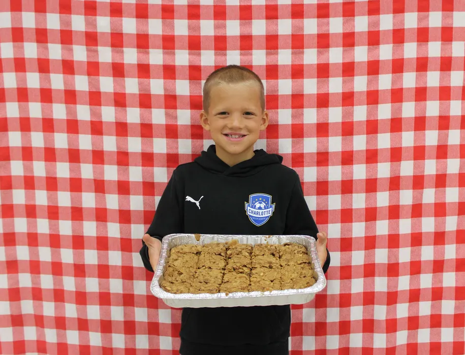 Boy stands in front of a red gingham background and smiles while holding a apple dish