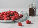 A plate of raspberries next to a jar of jam.