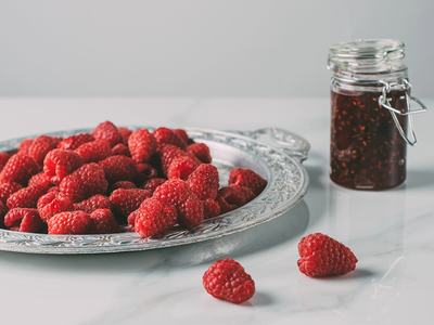 A plate of raspberries next to a jar of jam.