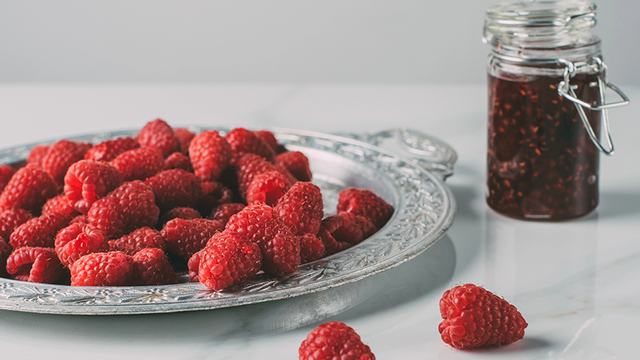 A plate of raspberries next to a jar of jam.