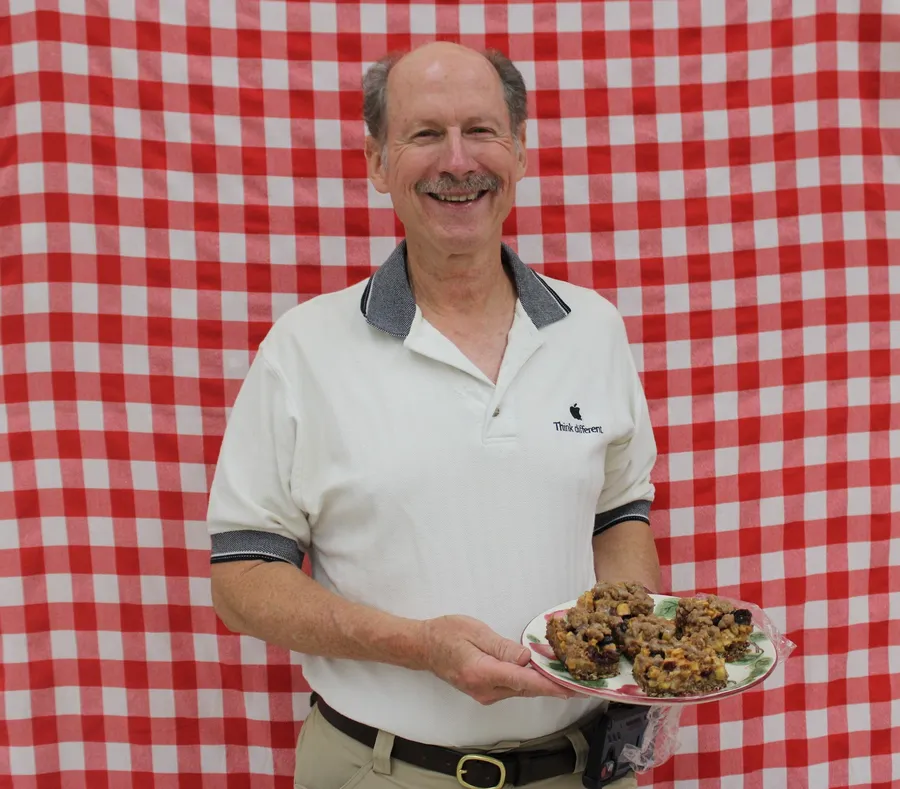 Man stands in front of a red gingham background and smiles while holding a apple dish