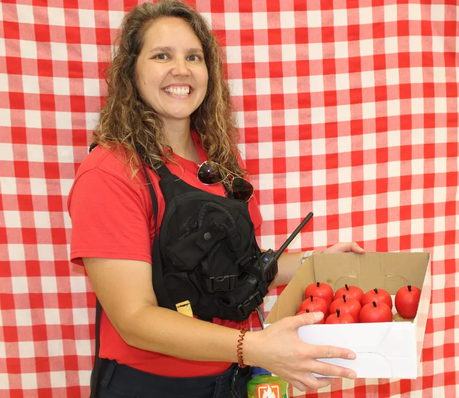 Woman stands in front of a red gingham background and smiles while holding a apple dish