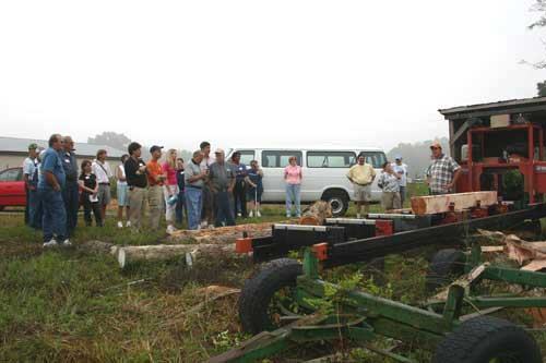 Group of people watching a portable sawmill cutting logs outdoors