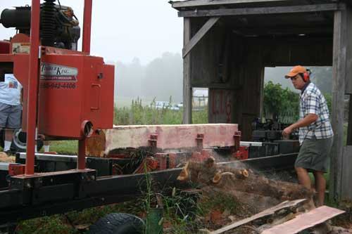 Man with ear protection operating portable sawmill cutting a log, sawdust flying