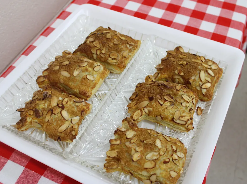 bear claw pastries sit displayed on a clear plastic dish on top of a red gingham tablecloth