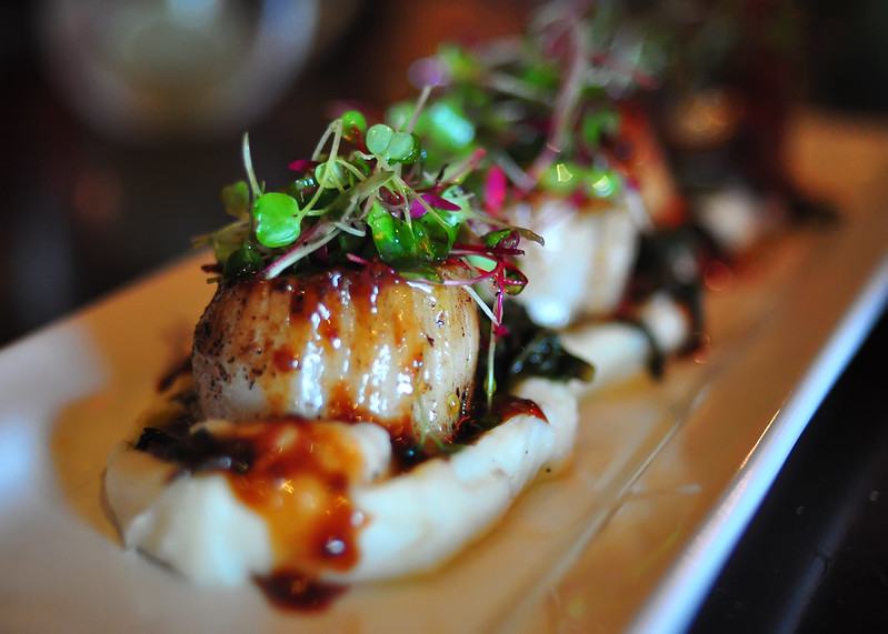 Microgreens as a garnish for scallops resting on mashed potatoes.
