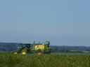 A green tractor in a field spraying pesticides