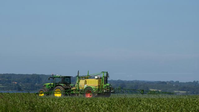 A green tractor in a field spraying pesticides