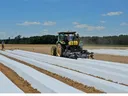 field covered in plastic. tractor with plastic layer attached on the back