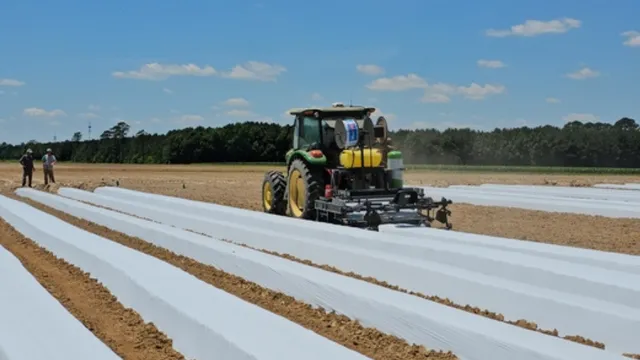 field covered in plastic. tractor with plastic layer attached on the back