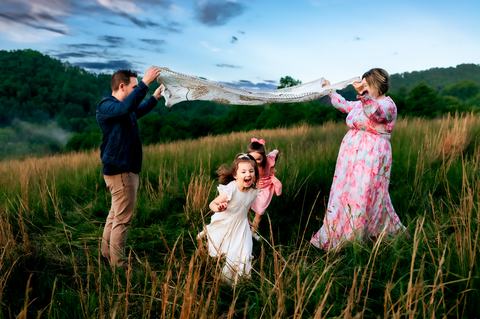 mom, dad, and two daughters playing with a blanket in a field with a backdrop of the appalachian mountains