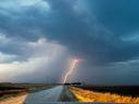 long stretch of road  with heavy  storm clouds and single lightening strike